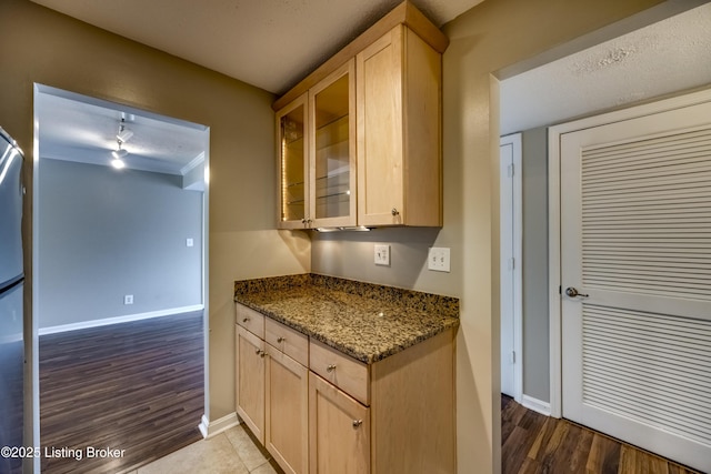 kitchen featuring dark stone countertops, light brown cabinets, glass insert cabinets, and baseboards