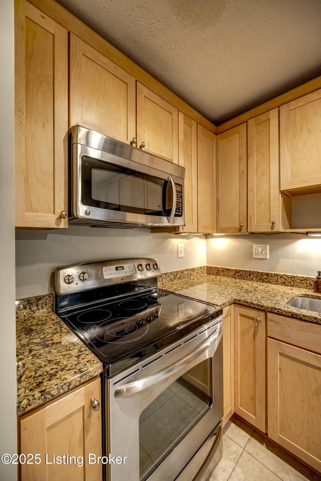 kitchen featuring light tile patterned floors, a textured ceiling, a sink, appliances with stainless steel finishes, and light stone countertops