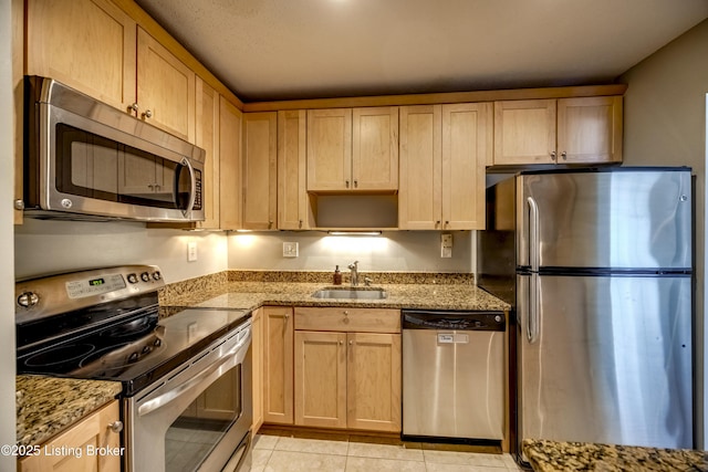 kitchen featuring stainless steel appliances, light tile patterned floors, a sink, and light stone countertops