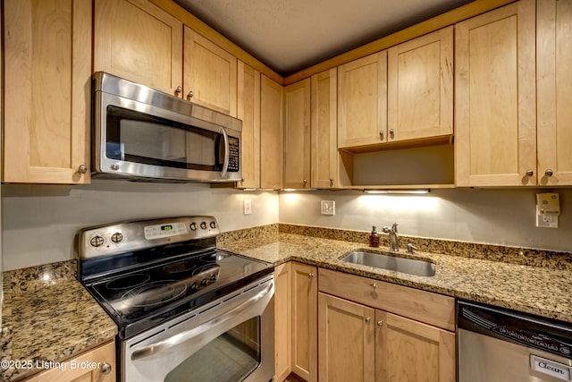 kitchen featuring light stone countertops, light brown cabinets, stainless steel appliances, and a sink