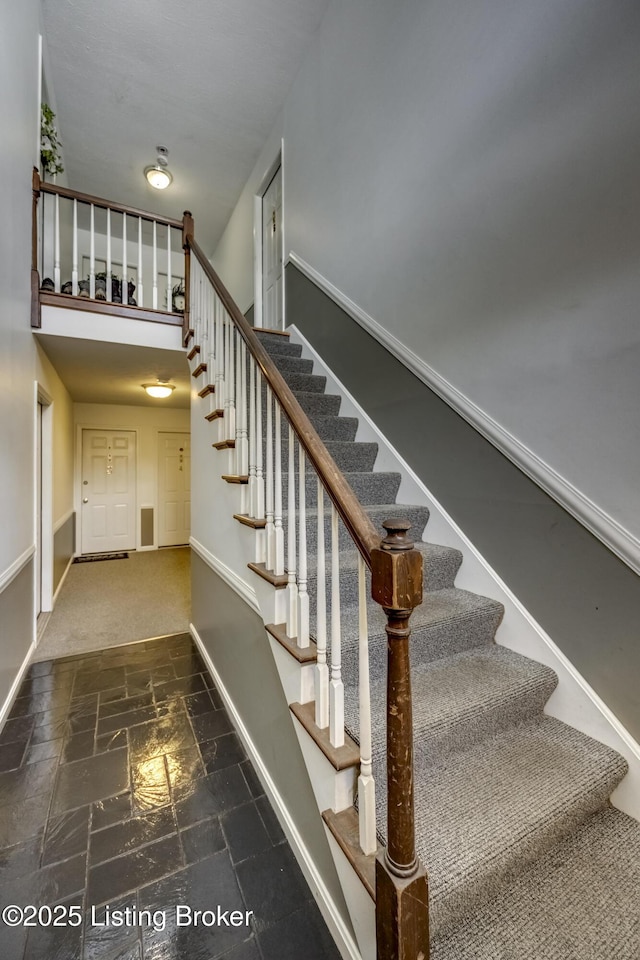 stairway with a towering ceiling, stone tile flooring, and baseboards