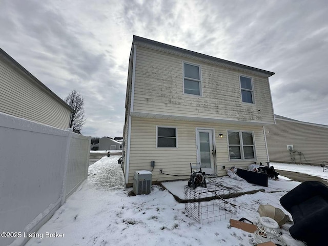 snow covered back of property featuring central air condition unit and fence