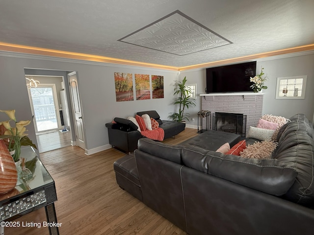 living area with ornamental molding, a brick fireplace, a textured ceiling, wood finished floors, and baseboards