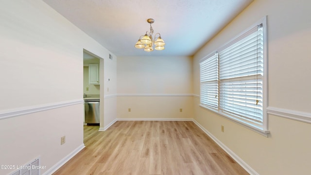 empty room featuring light wood-type flooring, baseboards, an inviting chandelier, and visible vents