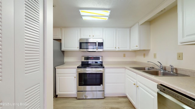 kitchen with a sink, light countertops, light wood-style floors, appliances with stainless steel finishes, and white cabinetry