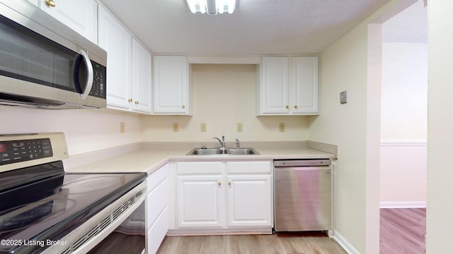 kitchen featuring light wood-type flooring, light countertops, appliances with stainless steel finishes, white cabinetry, and a sink