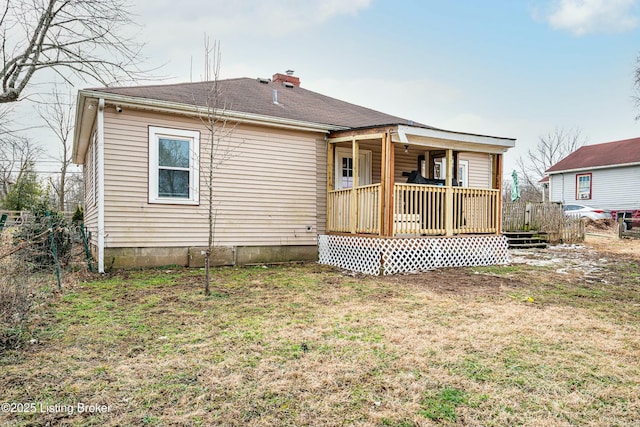 rear view of property with a deck, roof with shingles, a lawn, and a chimney