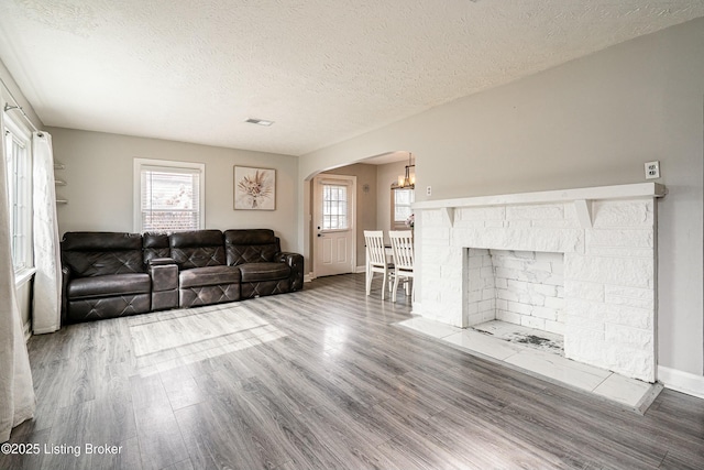 living area featuring arched walkways, a fireplace, light wood-style floors, a textured ceiling, and baseboards