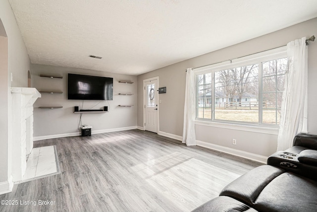 unfurnished living room featuring a fireplace with flush hearth, light wood-type flooring, a textured ceiling, and baseboards