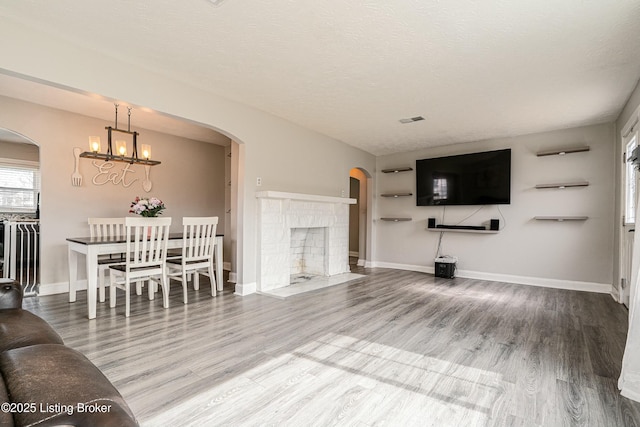 living room featuring arched walkways, visible vents, a textured ceiling, and wood finished floors