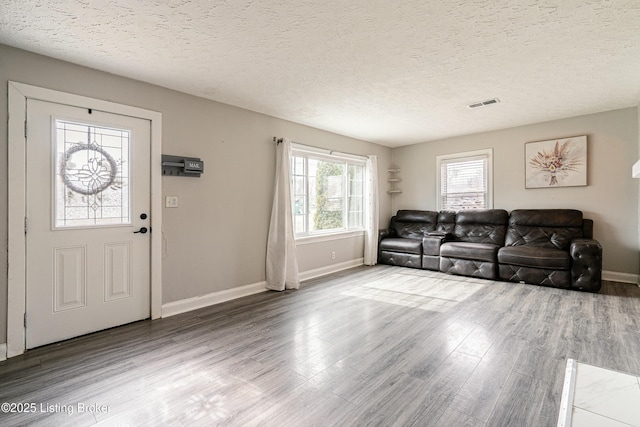 living area with a textured ceiling, wood finished floors, visible vents, and baseboards