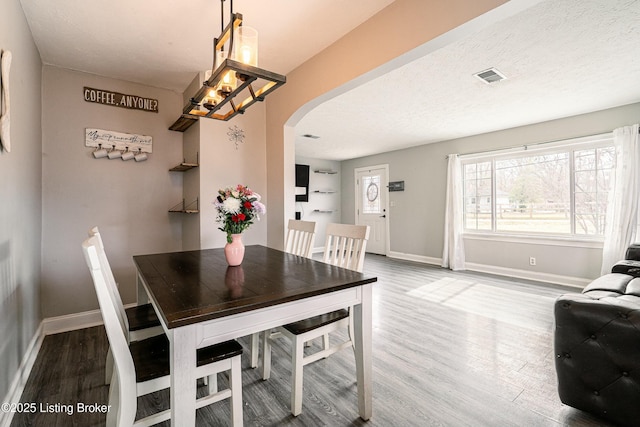 dining room featuring arched walkways, a textured ceiling, wood finished floors, visible vents, and baseboards