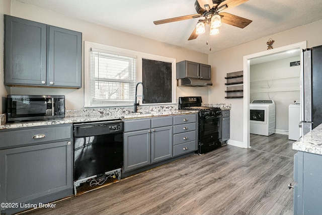 kitchen with a sink, washer and dryer, gray cabinets, dark wood-style floors, and black appliances