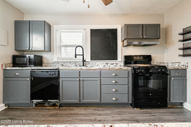 kitchen with dark wood finished floors, gray cabinets, a sink, under cabinet range hood, and black appliances