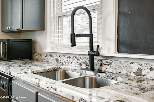 kitchen with light stone counters, a sink, gray cabinetry, and black appliances