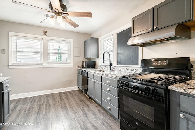 kitchen featuring a healthy amount of sunlight, under cabinet range hood, black appliances, and light stone countertops