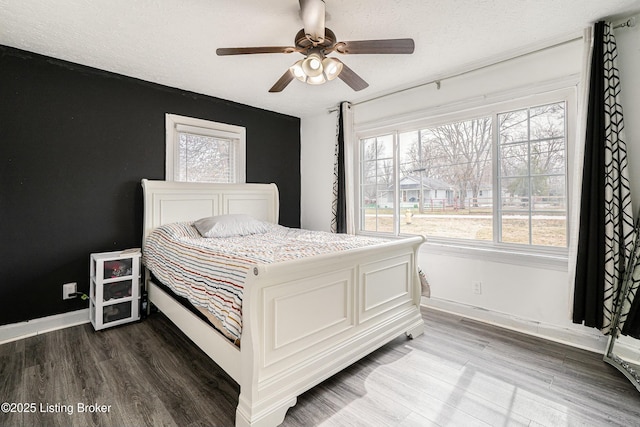 bedroom with a textured ceiling, multiple windows, wood finished floors, and baseboards