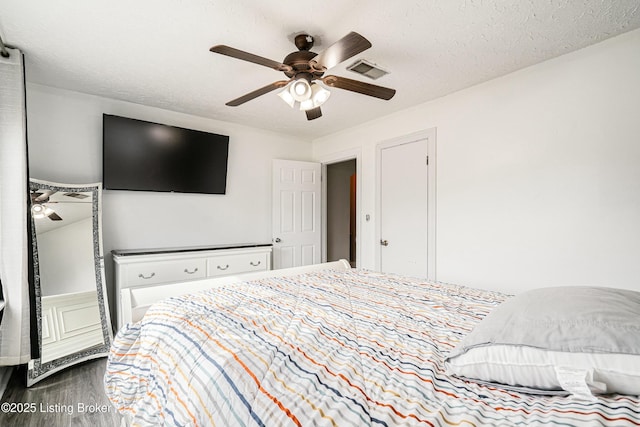 bedroom featuring ceiling fan, a textured ceiling, visible vents, and wood finished floors