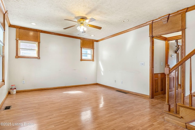 spare room with stairs, light wood finished floors, visible vents, and a healthy amount of sunlight