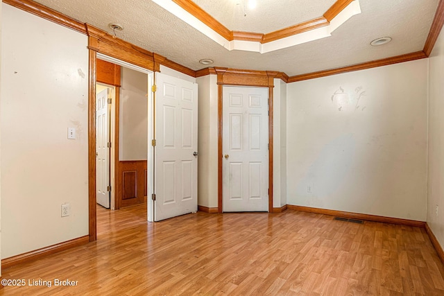 unfurnished bedroom featuring visible vents, light wood-style flooring, ornamental molding, a tray ceiling, and a textured ceiling