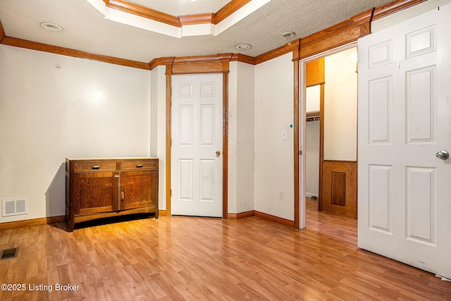 unfurnished bedroom featuring light wood-type flooring, visible vents, a textured ceiling, and ornamental molding