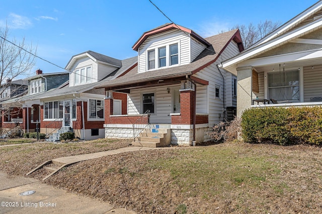 bungalow featuring a porch, roof with shingles, a front yard, and brick siding