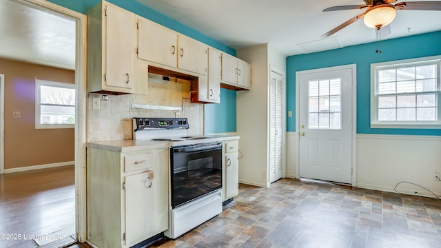 kitchen with tasteful backsplash, baseboards, electric range oven, stone finish flooring, and light countertops