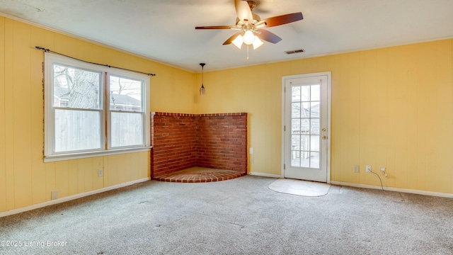 carpeted empty room featuring baseboards, crown molding, visible vents, and a ceiling fan