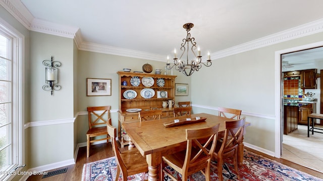 dining room with light wood finished floors, baseboards, visible vents, ornamental molding, and a chandelier