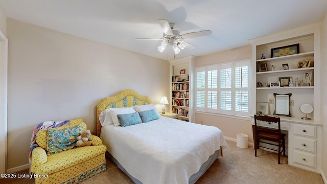 bedroom with light carpet, ceiling fan, built in desk, and baseboards