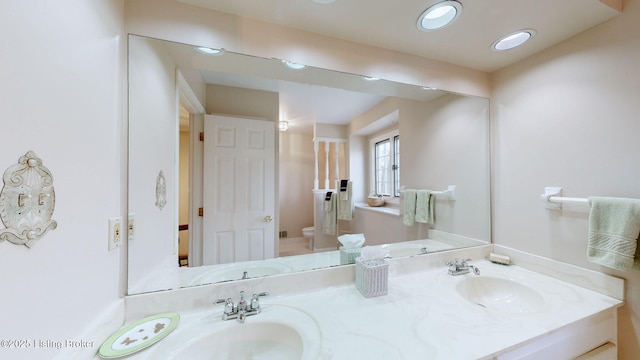 full bath with double vanity, a sink, toilet, and recessed lighting