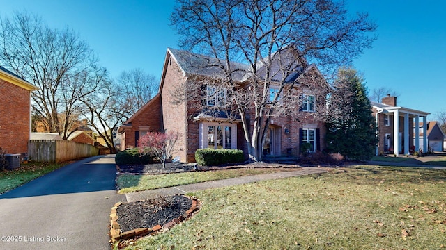 view of front of home with central AC, brick siding, a front lawn, and fence