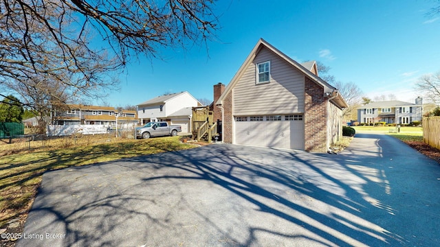 view of home's exterior with driveway, brick siding, an attached garage, and fence