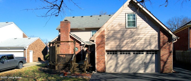 exterior space featuring a garage, a chimney, aphalt driveway, and brick siding