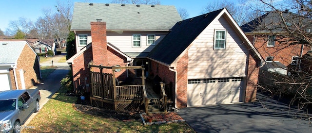 rear view of property featuring a garage, driveway, brick siding, and a chimney