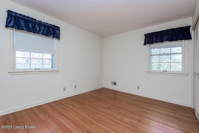 empty room with light wood-type flooring, visible vents, a textured ceiling, and baseboards