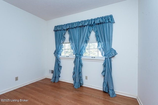 unfurnished room featuring wood finished floors, visible vents, and baseboards