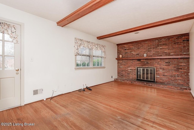 unfurnished living room featuring a brick fireplace, visible vents, beam ceiling, and wood finished floors