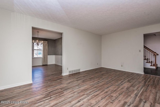 unfurnished room with a notable chandelier, visible vents, a textured ceiling, wood finished floors, and stairs