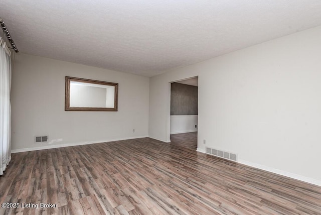 empty room with visible vents, a textured ceiling, baseboards, and wood finished floors