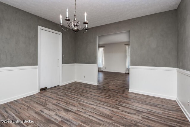 empty room with a chandelier, a wainscoted wall, and wood finished floors