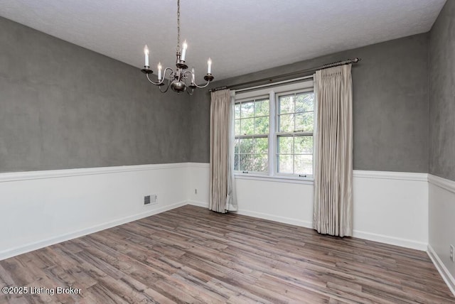 empty room with a textured ceiling, wood finished floors, visible vents, baseboards, and an inviting chandelier