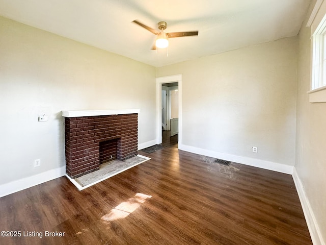 unfurnished living room with dark wood-style floors, visible vents, a brick fireplace, ceiling fan, and baseboards