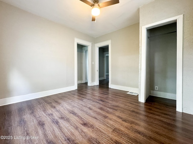 unfurnished bedroom featuring dark wood-style floors, visible vents, baseboards, and a ceiling fan