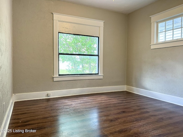 spare room featuring baseboards, dark wood-style flooring, and a textured wall