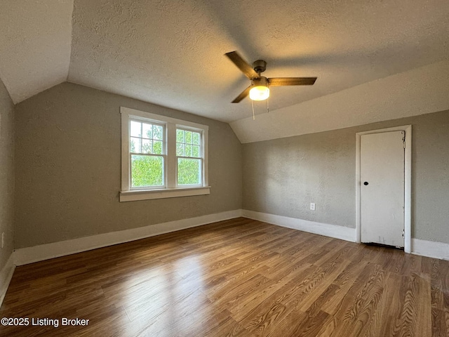 bonus room with baseboards, a textured wall, wood finished floors, vaulted ceiling, and a textured ceiling