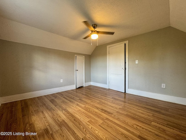 interior space featuring lofted ceiling, light wood finished floors, baseboards, and a textured ceiling