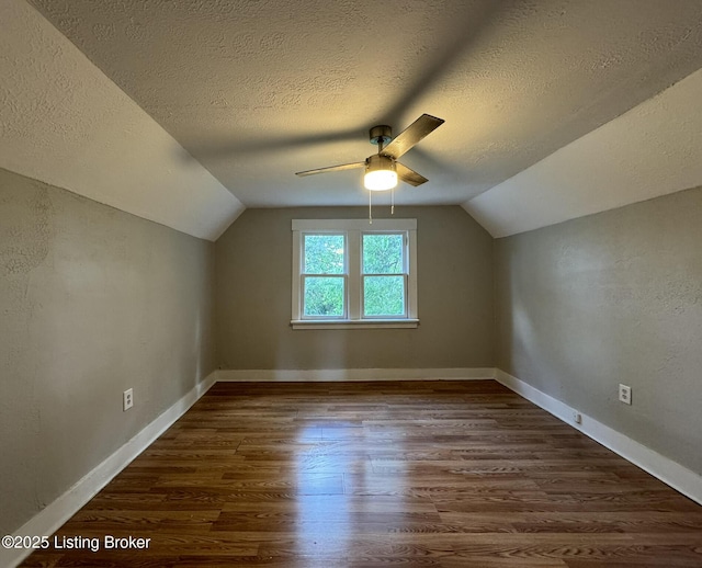 additional living space with dark wood-style floors, vaulted ceiling, and a textured ceiling