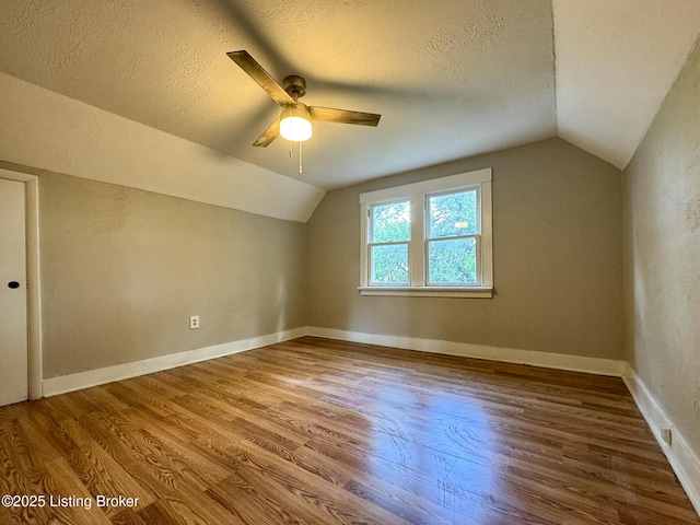 bonus room with a textured ceiling, vaulted ceiling, wood finished floors, and baseboards