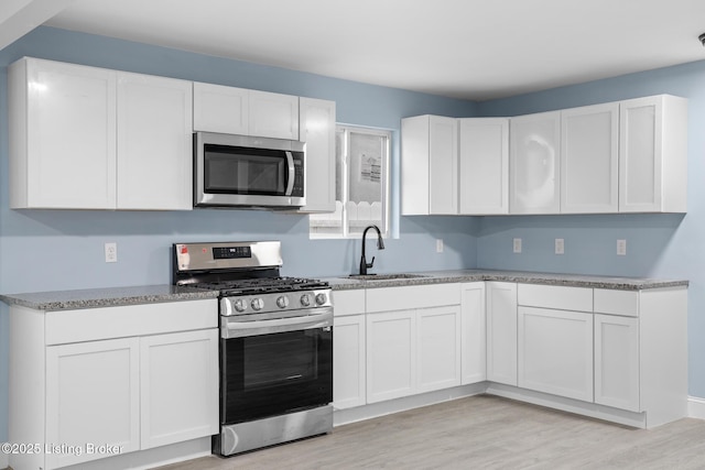 kitchen featuring appliances with stainless steel finishes, white cabinetry, and a sink